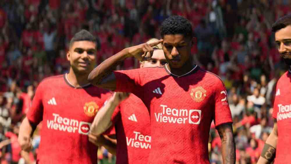Marcus Rashford in a red Man United shirt pointing to his head with his finger. 