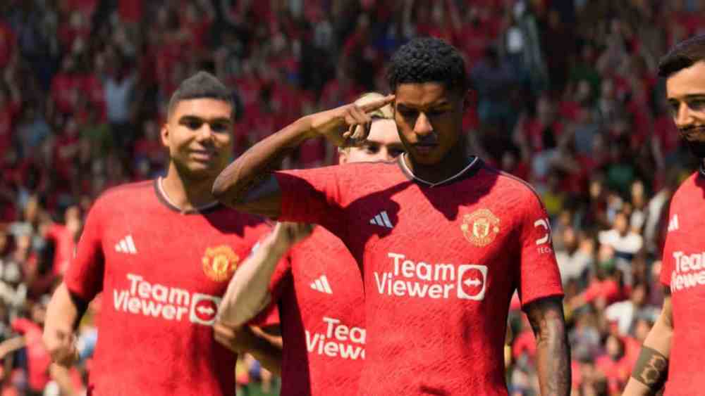 Marcus Rashford in a red Man United shirt pointing to his head with his finger.